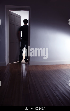Back view of a shadowy male walking out of a dark room. Stock Photo