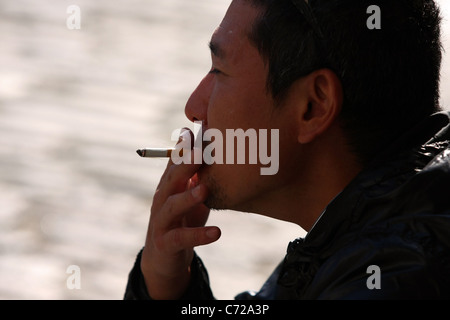 A man (sitting on the ground) puffing on a lighted cigarette Stock Photo