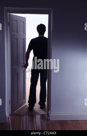 Back view of a male figure entering a well lit room leaving a dark room Stock Photo