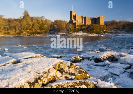 Dunvegan Castle on the shore of Loch Dunvegan, above frozen sea ice and hoar frost on rocks Stock Photo