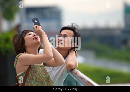 A young Chinese couple taking photos in Hong Kong with an Apple iPhone 4 smartphone. Stock Photo
