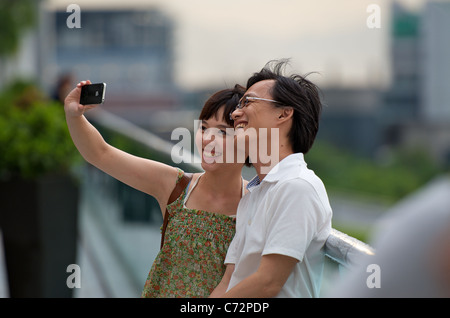 A young Chinese couple taking selfie photos in Hong Kong with an Apple iPhone 4 smartphone. Stock Photo