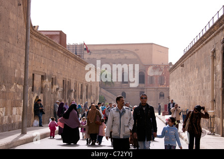 Visitors walking in a large corridor inside the Saladin Citadel in Cairo, Egypt. There are buildings on all sides and people Stock Photo