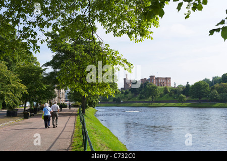Elderly couple walking along  path on banks of the River Ness with the Castle in the distance, Inverness, Highland, Scotland, UK Stock Photo