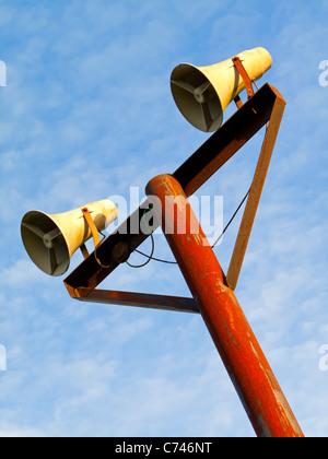Pair of public address system loudspeakers on a pole with blue sky behind Stock Photo