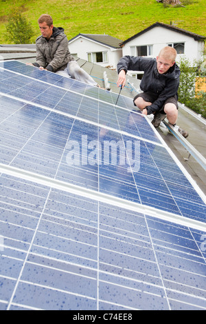 Workers installing solar electric panels on a house roof in Ambleside, UK. Stock Photo