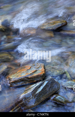 Water flowing amidst the colorful rocks of the Haast River in Haast Pass, New Zealand Stock Photo