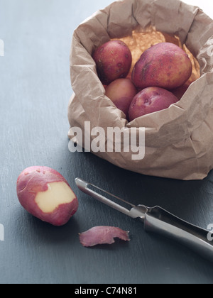 Red baby potatoes in bag with peeler and one partially peeled potato Stock Photo