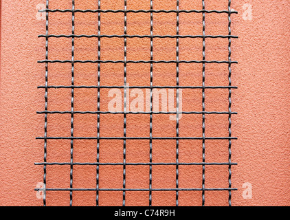Black wire grid against a salmon stucco wall Stock Photo