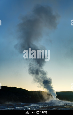 Old Faithful geyser erupting under early morning twilight sky, Yellowstone National Park, Wyoming, USA Stock Photo