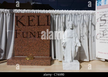 A small statuette of Jesus stands in bright sunlight in a funeral parlour's front window. Stock Photo