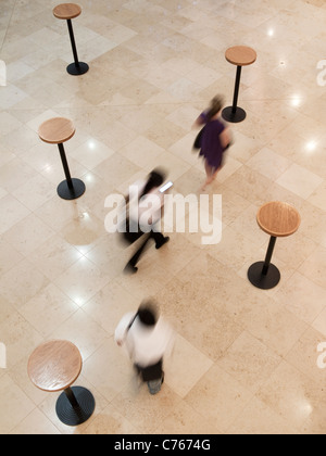 A view from above of three blurred people walking amongst five tables on the concert level in Kings Place, London. Stock Photo