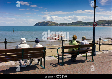 Two couples of senior citizens sit on benches, looking out to sea, watching passengers board two small pleasure boats. Stock Photo