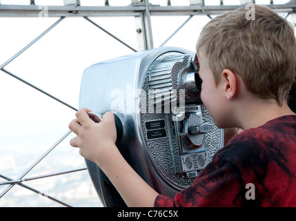 A boy looking through coin operated binoculars at the top of the Empire State Building, New York USA Stock Photo