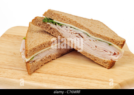 Turkey and cheese sandwich on whole meal bread cut in half on wood cutting board on white background. Stock Photo