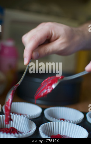 Spooning red cupcake mixture/batter into paper baking cases. Stock Photo