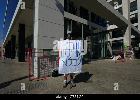 A protester holds a paperboard sign in Hebrew which reads 'Shari Arison to Jail' in front of Bank Hapoalim controlled by Arison Holdings, which is owned by Shari Arison in Tel Aviv Israel. The social justice protest also named the Tents protest were a series of demonstrations in Israel beginning in July 2011 involving hundreds of thousands of protesters from a variety of socio-economic opposing the continuing rise in the cost of living particularly housing. Stock Photo