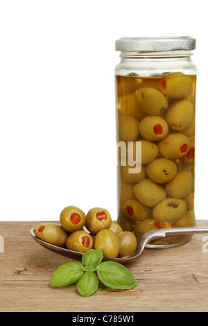 Olives in a spoon with a jar of olives and basil herb on an old wooden board Stock Photo