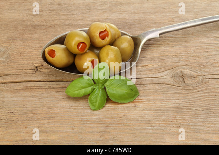 Stuffed olives in silver spoon with a sprig of basil on old rustic wood Stock Photo