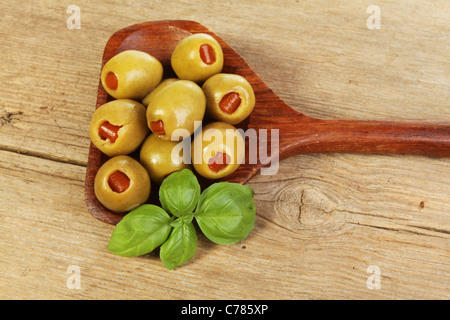 Olives in a wooden spoon with a sprig of basil on old weathered wood Stock Photo
