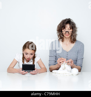 Studio shot of mother knitting and daughter (10-11) using handheld video game Stock Photo