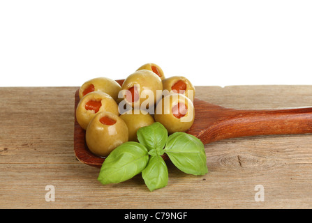 Olives and a sprig of fresh basil in a wooden spoon on old weathered wood against a white background Stock Photo