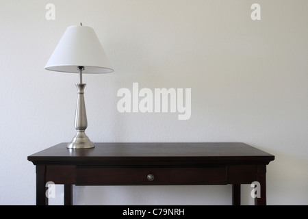 silver table lamp sitting on a wooden table with a white wall in the background and copy space Stock Photo