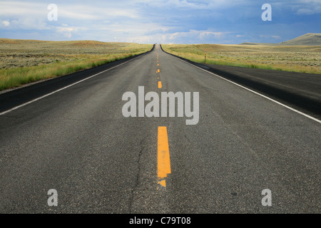 a car crests the distant hill on an empty road in Wyoming