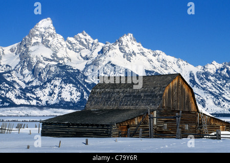 An old weathered barn is dwarfed by the snow-covered Grand Teton Mountains in wintertime in Jackson Hole, Wyoming, USA. Stock Photo