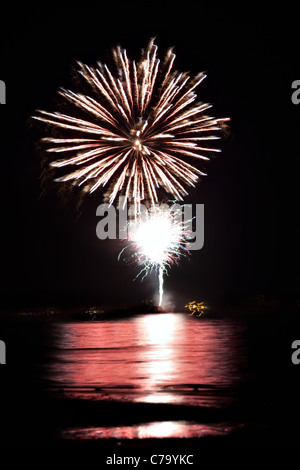 Beautiful fireworks going off over the dark night sky reflecting over the water. Stock Photo