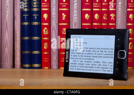 A black e book reader on a shelf with classical books. Stock Photo