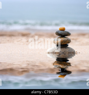 A pile of round smooth zen like stones stacked in the sand at the beach. Stock Photo