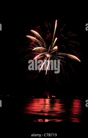 Beautiful fireworks going off over the dark night sky reflecting over the water. Stock Photo