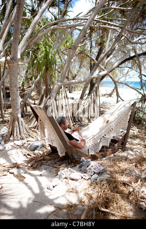 Guest in the hammock right at the beach under Pandanus trees Wilson Island Resort Wilson Island part of the Capricornia Cays Nat Stock Photo