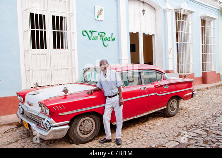 Man standing in front of his red vintage American car (Chevrolet) in front of Via Reale, Trinidad, Sancti Spiritus, Cuba Stock Photo