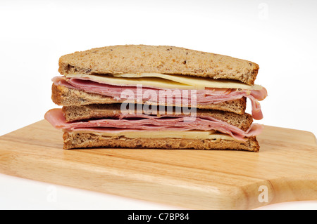Ham and cheese sandwich on whole meal bread cut in half on wood cutting board on white background. Stock Photo