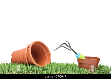 A studio shot of flower pots and a rake on a green grass Stock Photo