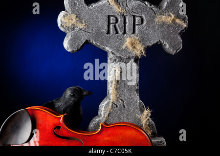 A Halloween violin viola with a blackbird crow and gravestone against a dark blue spotlight background. Stock Photo