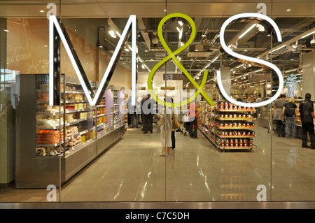 M&S retail business sign mounted on glass window of foodhall in Marks and Spencer store in Westfield Shopping Centre shoppers in food shop London UK Stock Photo