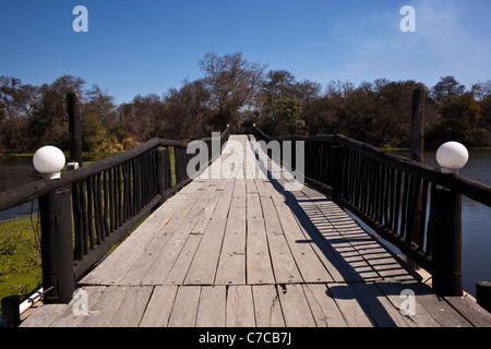 A wooden bridge over a river with trees and blue sky in the background
