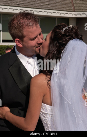 Couple first kiss during Catholic wedding ceremony held outside during sunny summer day vertical in USA US hi-res Stock Photo