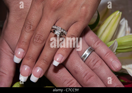 Newly married young interracial couple showing off their hands with wedding rings with brides wedding bouquet in the background in USA US hi-res Stock Photo