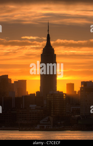 The rising sun shines from behind the Empire State Building just after sunrise in New York City. Stock Photo