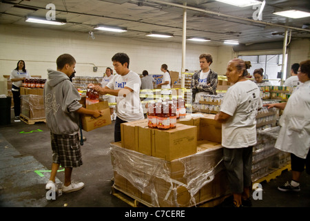 Hispanic and Caucasian volunteers give food to a young man at a charity food distribution in Santa Ana, CA. Note logo T-shirt. Stock Photo