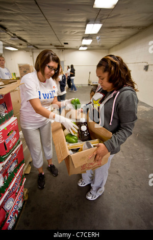 A Caucasian volunteer distributes free food to a Hispanic woman at a charity warehouse in Santa Ana, CA. Note charity T-shirt. Stock Photo