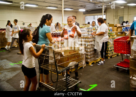 Hispanic and Caucasian volunteers give food to a young mom and her daughter at a charity food distribution in Santa Ana, CA. Stock Photo