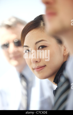 Young woman between two colleagues, all dressed up well in business style, looking at camera and smiling Stock Photo