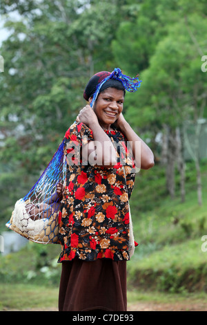 Mother carries her baby boy in a traditional woven bilum hanging from her head, Papua New Guinea Stock Photo
