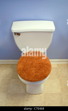 A modern looking toilet with a fuzzy, orange toilet seat cover. Stock Photo