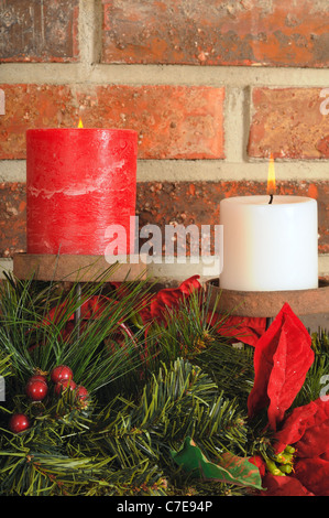 Two festive Christmas candles with greenery on a mantel with brick background Stock Photo